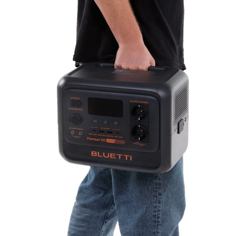 Tragbare Powerstation Bluetti Premium 100 in Schwarz-Grau mit orangefarbenen Akzenten, getragen von einer Person in einem schwarzen T-Shirt und einer blauen Jeans, mit verschiedenen Anschlüssen und Anzeigen auf der Vorderseite.