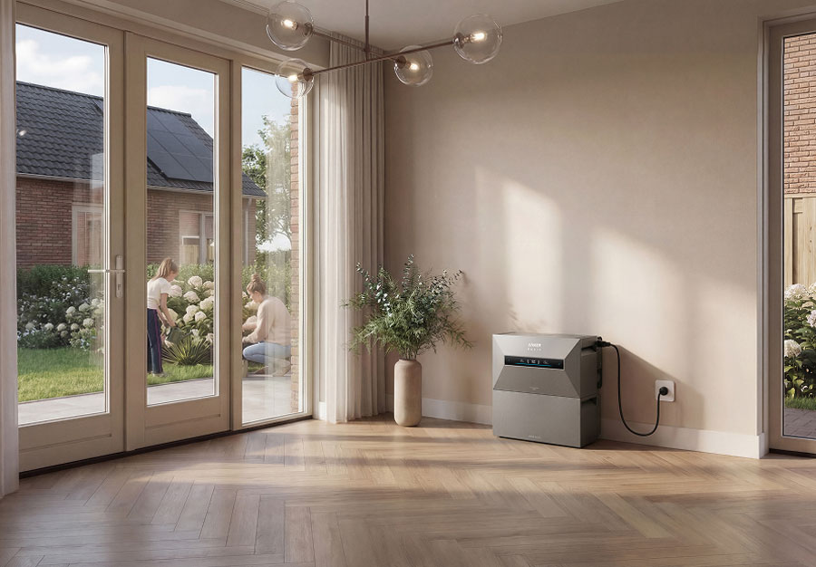 thuisbatterij grijs model van env-offgridpowerstationditistestnl-stg.kinsta.cloud in lichte woonkamer naast glazen schuifdeur met tuin en mensen die buiten planten verzorgen