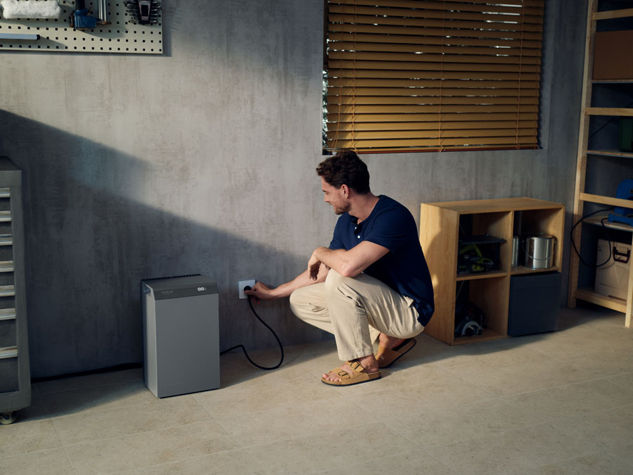 Tragbare Stromstation, graues Modell in einer Garage, in der ein Mann den Stecker in die Steckdose steckt; kompaktes Design, geeignet für die netzunabhängige Stromversorgung